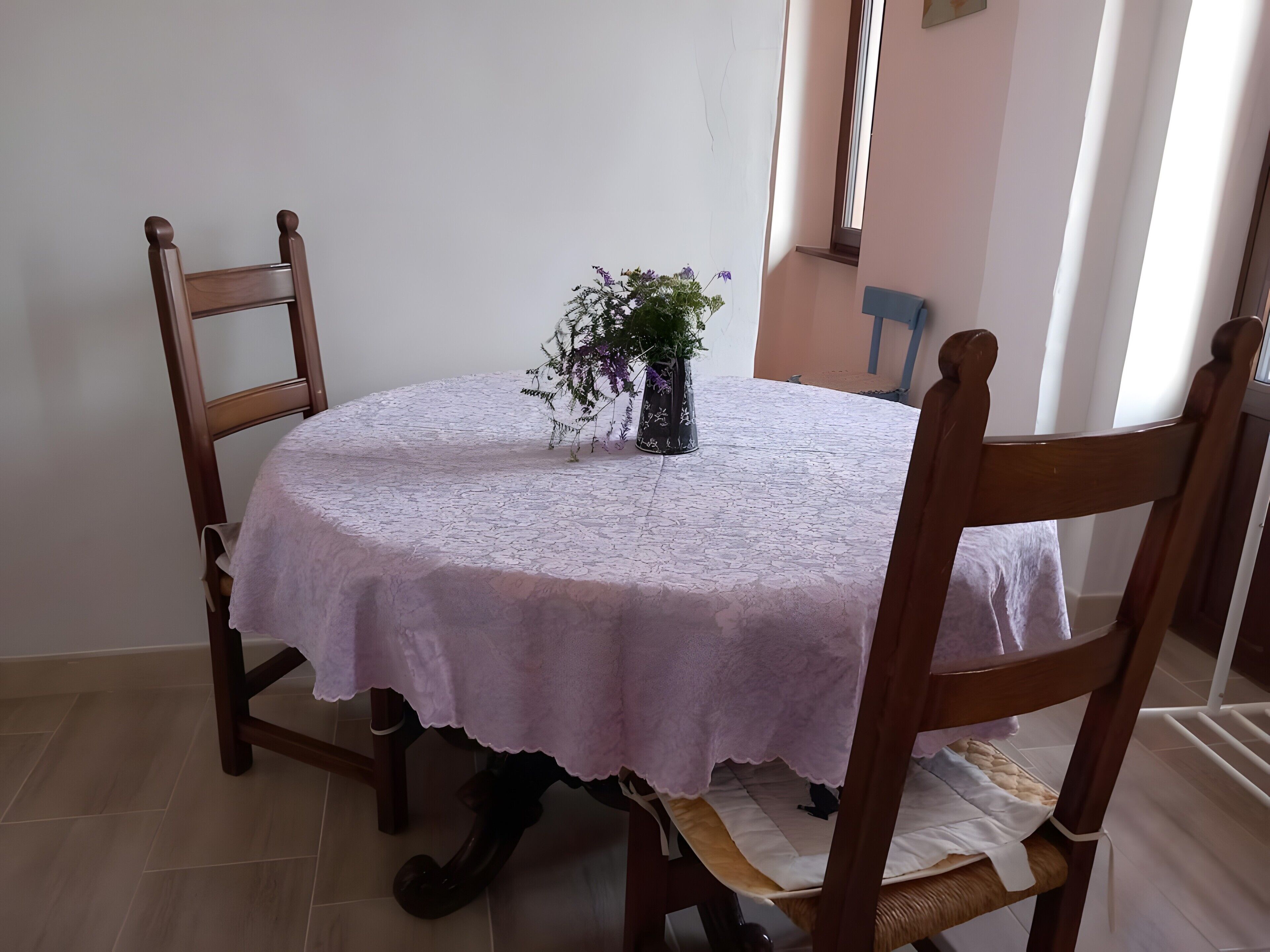Ein runder Esstisch mit Spitze, umgeben von hölzernen Stühlen mit gepolsterten Sitzflächen.