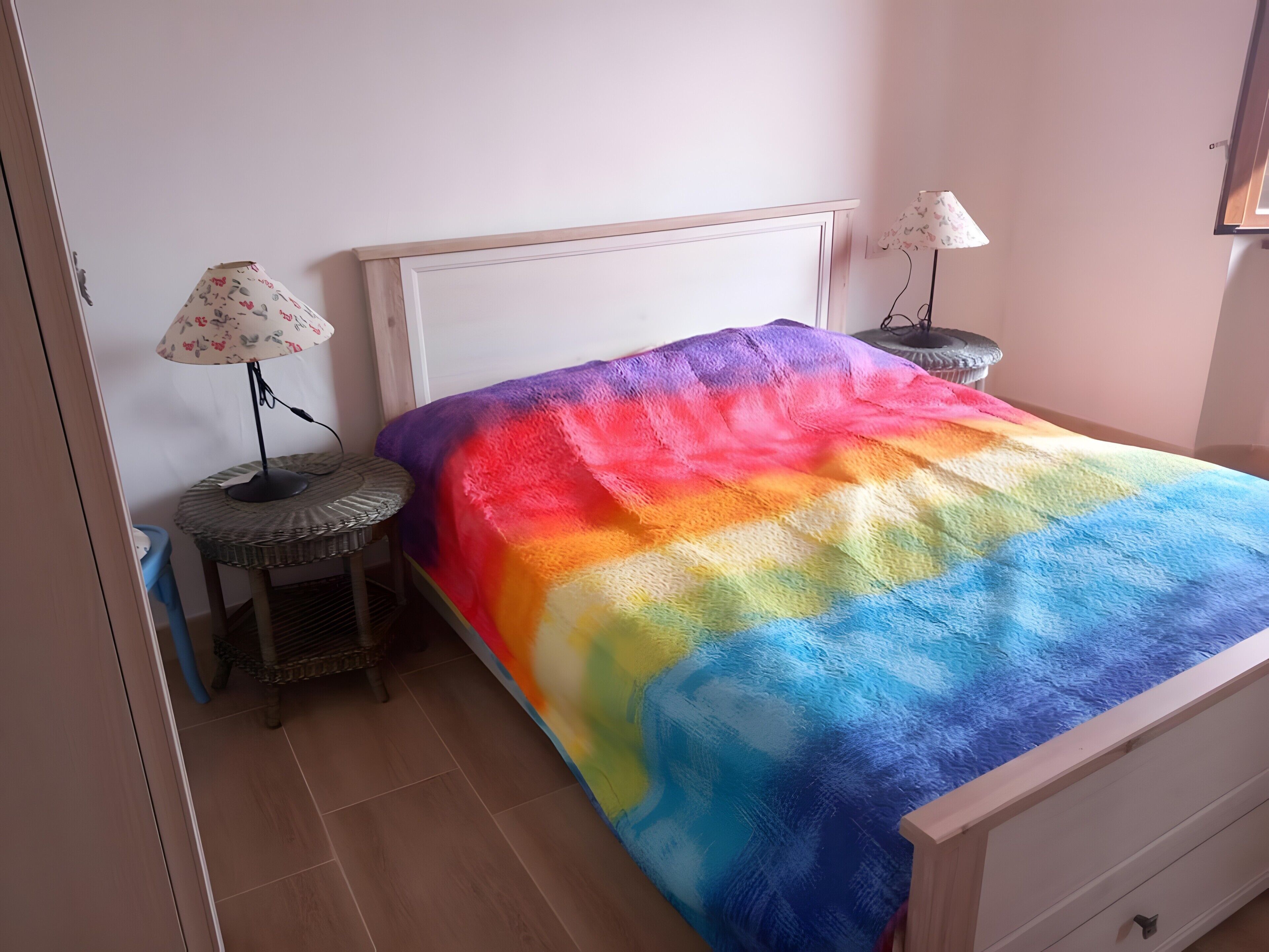 Ein Bett mit einer mehrfarbigen Decke, ein Nachttisch mit Lampe und ein kleiner runder Tisch mit einem Stuhl.