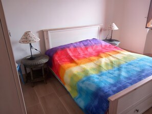 A bed with a rainbow-colored blanket, a bedside table with a lamp, and a small round table with a chair. - Apartment 'Artist Lake House with Panoramic' with Lake View, Private Terrace and Wi-Fi (Garabiolo)
