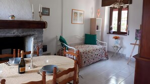 Habitació amb llar de foc, taula de menjador amb cadires, llit amb almoina verda, finestra amb vista i prestatgeria.