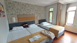 Et hotelværelse med to senge, trægulv og et vindue med gardiner.