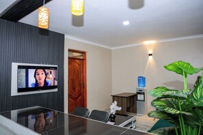 A modern meeting room with a flat-screen TV, a glass-top table, and a water dispenser. - 1 Bedroom Apartment in Utawala Nairobi  Near JKIA Free Wi-Fi & Parking (Nairobi)
