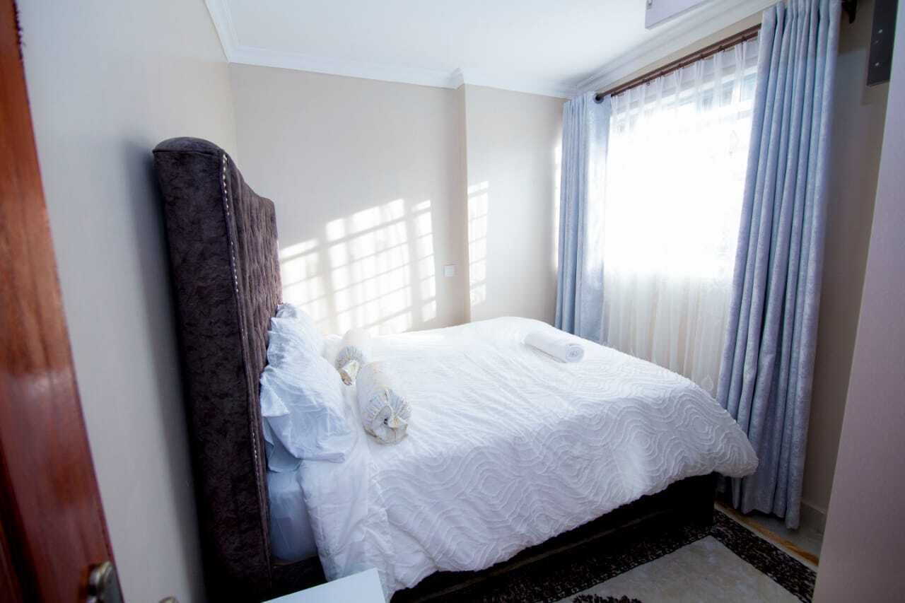 Ein Hotelzimmer mit Bett, Holz-Kopfteil, Fenster mit Vorhängen und einer Tür.