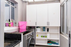 Eine kleine Küche mit weißen Schränken, einer Waschmaschine und einem rosa Eimer auf der Arbeitsfläche.