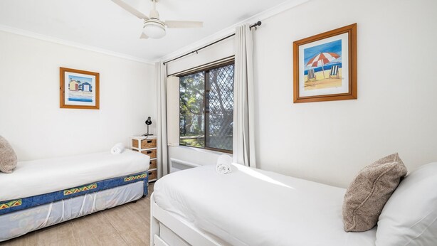 Quarto de hotel com duas camas, uma janela com vista para árvores e duas fotografias emolduradas nas paredes.