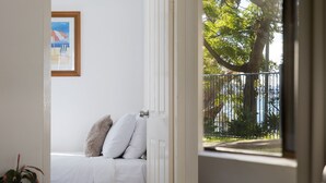 Quarto com uma cama, um quadro na parede e vista de uma árvore e cerca por uma porta aberta.