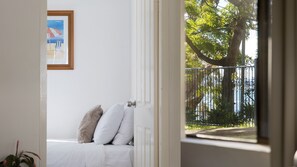 A room with a bed, a framed picture on the wall, and a view of a tree and fence through an open door. - The Poplars Apartment with views and  Swimming Pool (Nelson Bay)