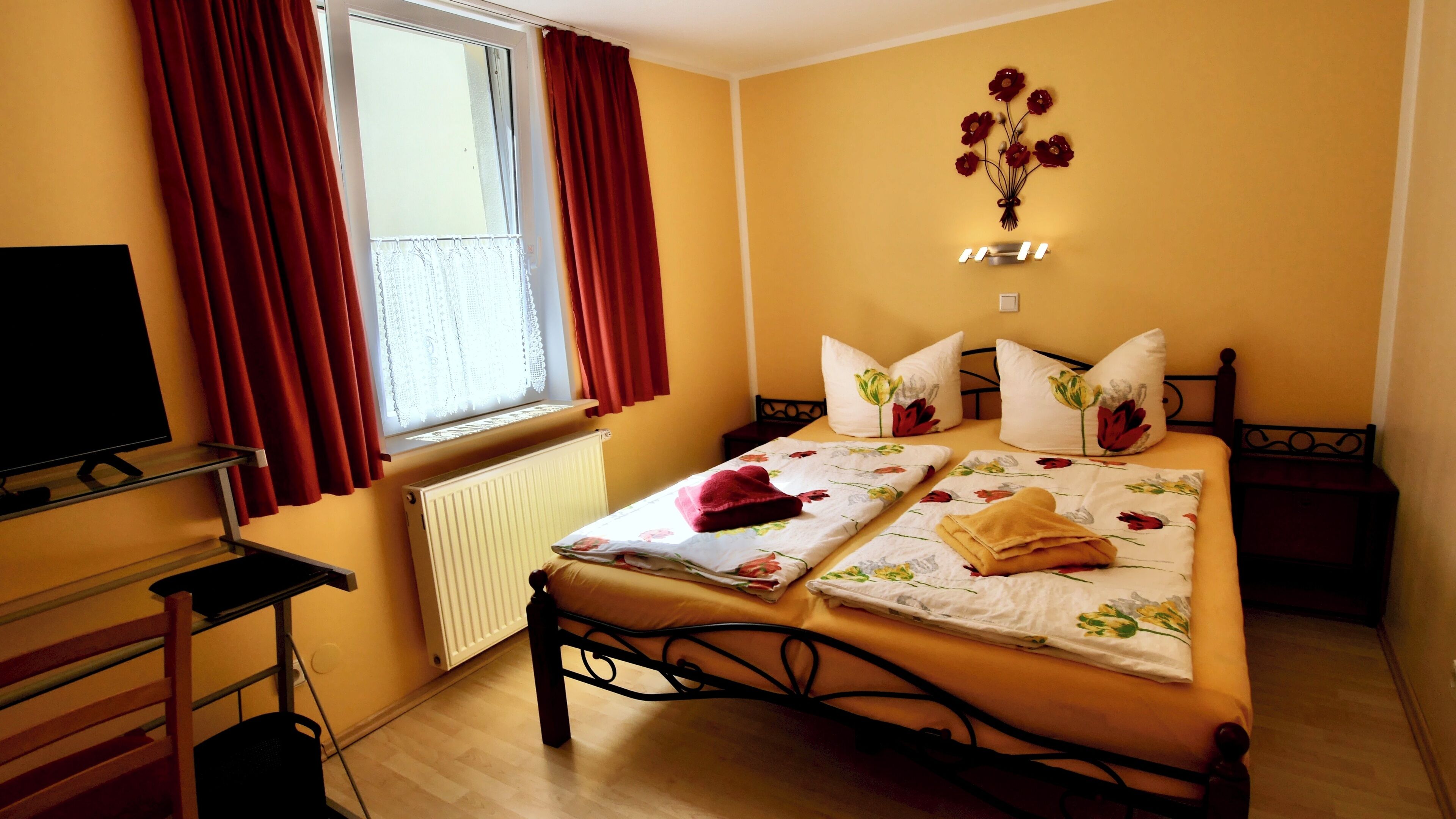 Ein Hotelzimmer mit Bett, Fernseher, Fenster mit Vorhängen, Heizkörper und Wandbild.
