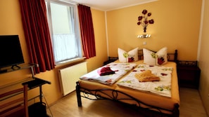 A hotel room with a bed, a TV, a window with curtains, a radiator, and a wall decoration. - Vrbo Property (Eisenach)