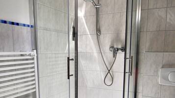 Ein modernes Badezimmer mit einer gläsernen Duschkabine, einer weißen Toilette und einer Sitzbank mit einem Handtuch.