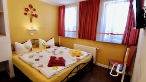 Una habitación de hotel con cama, radiador, silla y ventana con cortinas.