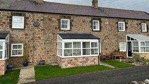 A stone house with multiple windows, a chimney, and a small garden area with a bench and potted plants. - Cottage - Sleeps 5 - Parking & Wood Burning Stove (Alnwick)