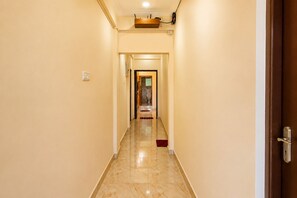 Un pasillo de hotel con suelo de mármol, una puerta de madera a la derecha y vista a una habitación con cama y ventana.