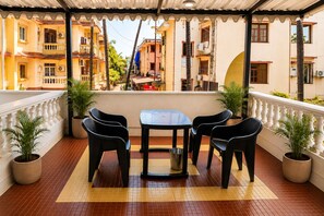 Un balcón con mesa y sillas, plantas en macetas y vista a una calle con edificios.