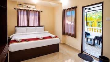 A hotel room with a bed, a desk, a chair, an air conditioning unit, and a view of the outside.