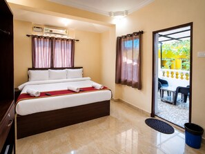 Habitación de hotel con cama, escritorio, silla, equipo de aire acondicionado y vista al exterior.