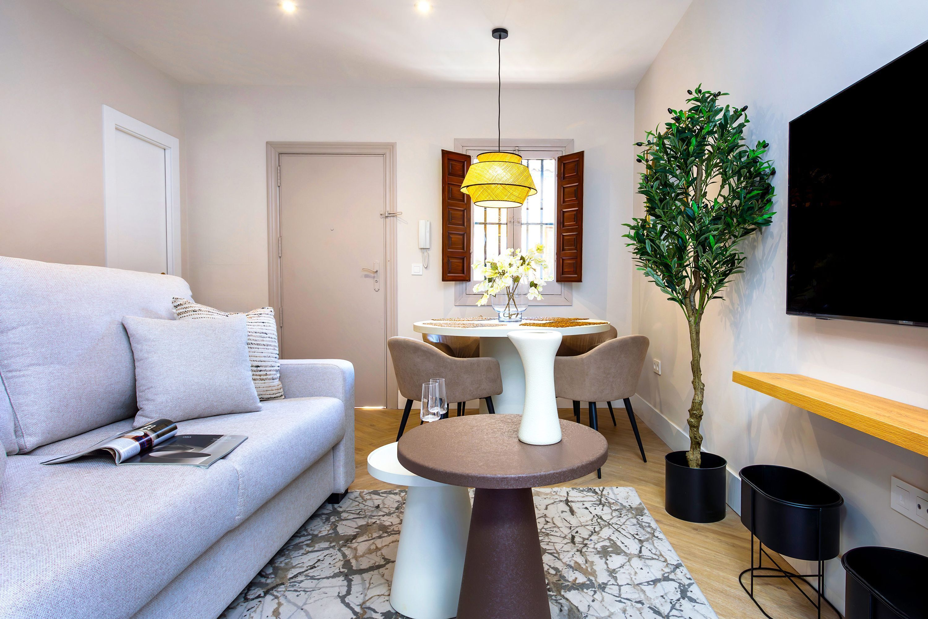 Un salon moderne comprenant un canapé, une table à manger avec des chaises, une plante en pot et un téléviseur à écran plat fixé au mur.