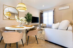 A modern living room with a round dining table, two chairs, a sofa, a TV, and a large mirror. - Genteel Home Santa Ines (Granada)