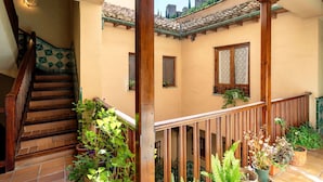 A multi-level interior with a wooden staircase, a balcony with potted plants, and a view of the outside. - Genteel Home Santa Ines (Granada)