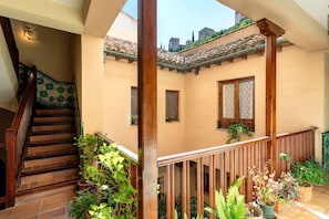 Ein mehrgeschossiges Interieur mit einer Holztreppe, einem Balkon mit Topfpflanzen und Blick ins Freie.