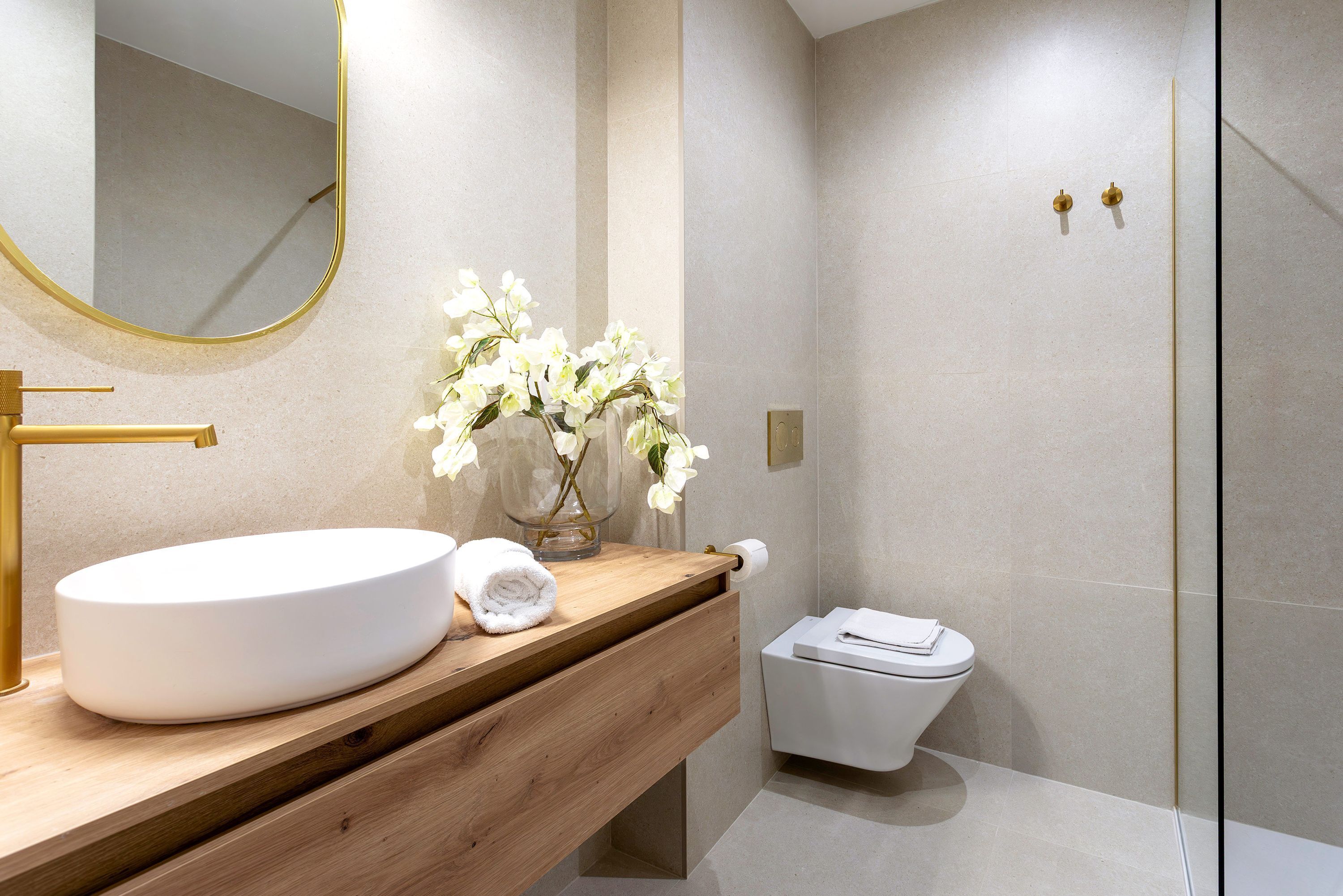 A modern bathroom with a wooden vanity, a white sink, a mirror with a gold frame, and a toilet.