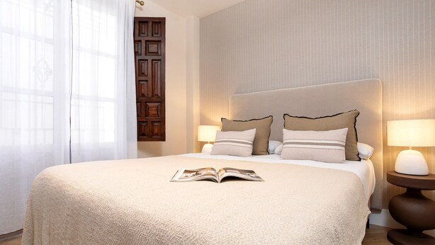 A hotel room with a large bed, two bedside lamps, a wooden door, and a window with sheer curtains. - Genteel Home Santa Ines (Granada)