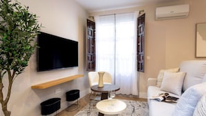 A modern living room with a flat-screen TV, a round coffee table, a sofa, a potted plant, and a window with curtains. - Genteel Home Santa Ines (Granada)