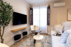 Ein modernes Wohnzimmer mit Flachbildfernseher, rundem Couchtisch, Sofa, Topfpflanze und einem mit Vorhängen versehenen Fenster.