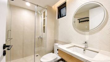 A modern bathroom with a glass shower enclosure, a toilet, a sink with a mirror, and a small window.