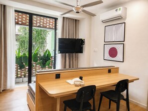 A modern room with a wooden desk, two black chairs, a ceiling fan, an air conditioning unit, and a TV mounted on the wall. - CityHouse NEST Dien Bien Phu (Ho Chi Minh City)