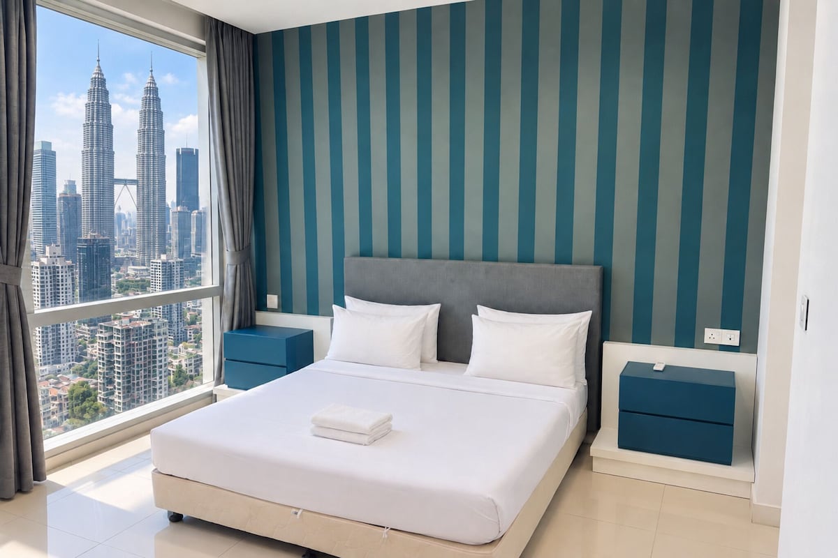 A hotel room with a large bed, two bedside tables, a view of the cityscape, and striped walls.