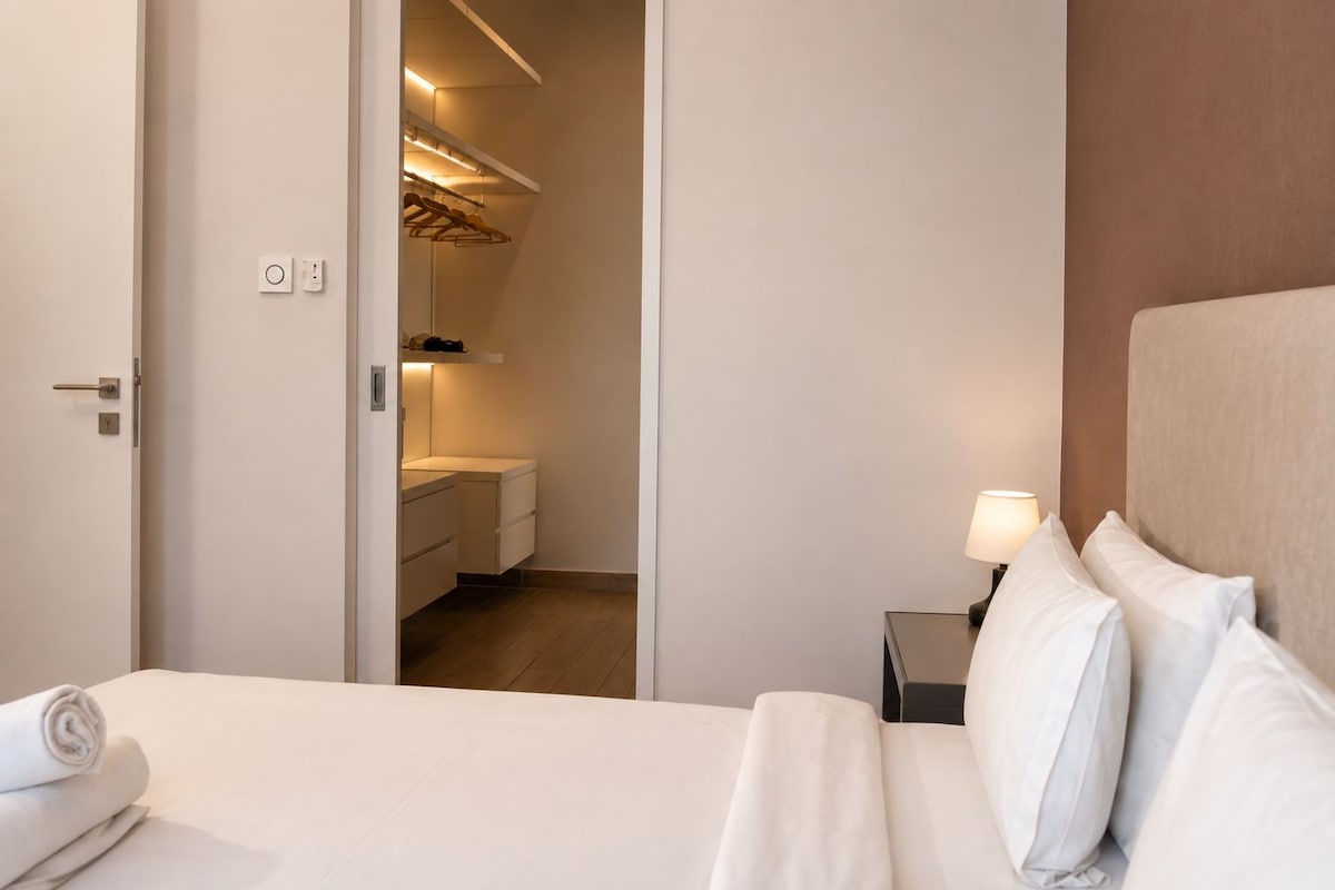 A hotel room with a bed, a nightstand with a lamp, a wardrobe, and a bathroom visible through an open door.