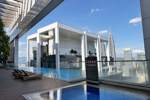 A rooftop pool area with a glass barrier, lounge chairs, and a view of the city skyline. - Platinum Suites KLCC by Moonlight (Kuala Lumpur)