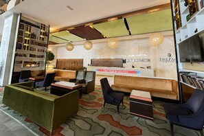 Um saguão de hotel com balcão de recepção, área de estar e uma estante de livros.