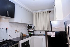 A kitchen with white cabinets, a black refrigerator, a stove, and a sink. - Cosy 1BR Apartment with Balcony, Free Wi-Fi & Secure Parking (Nairobi)
