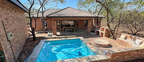 A swimming pool with a brick deck, a covered patio area, and a brick house in the background.