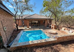 Una piscina con solárium de ladrillo, un porche cubierto y una casa de ladrillo al fondo.