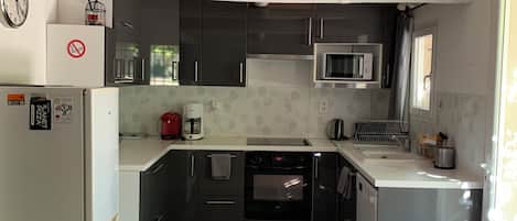 A compact kitchen with a refrigerator, microwave, oven, and a coffee maker.