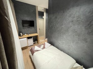 A hotel room with a bed, a desk with a flat-screen TV, a small kitchenette, and a wardrobe.
