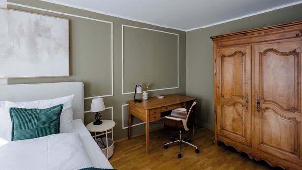 Habitación de hotel con cama, escritorio, silla, armario y obras de arte en la pared.