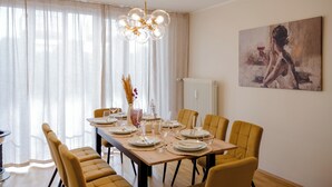Comedor con mesa dispuesta para seis personas, sillas, una araña y un cuadro en la pared.