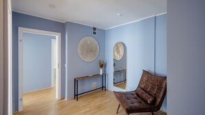 Una habitación con piso de madera, un sillón de cuero marrón, una puerta blanca y dos espejos redondos colgados en la pared.