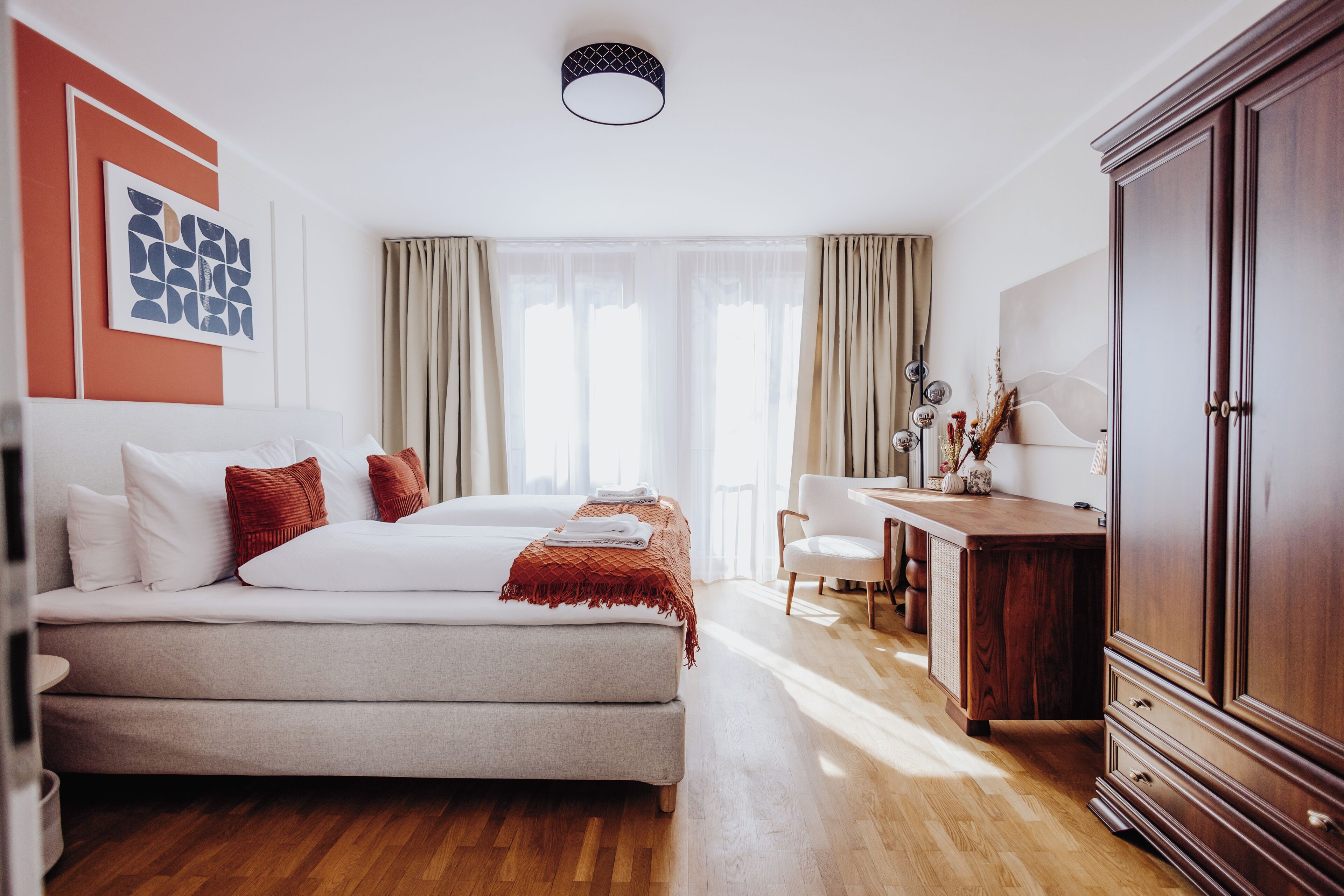 Une chambre d’hôtel avec un lit, un bureau, une armoire et une grande fenêtre avec des rideaux.