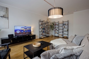 Una sala moderna con un televisor de pantalla plana, un mueble de entretenimiento negro, una gran mesa de centro negra, un sofá gris y una planta decorativa.