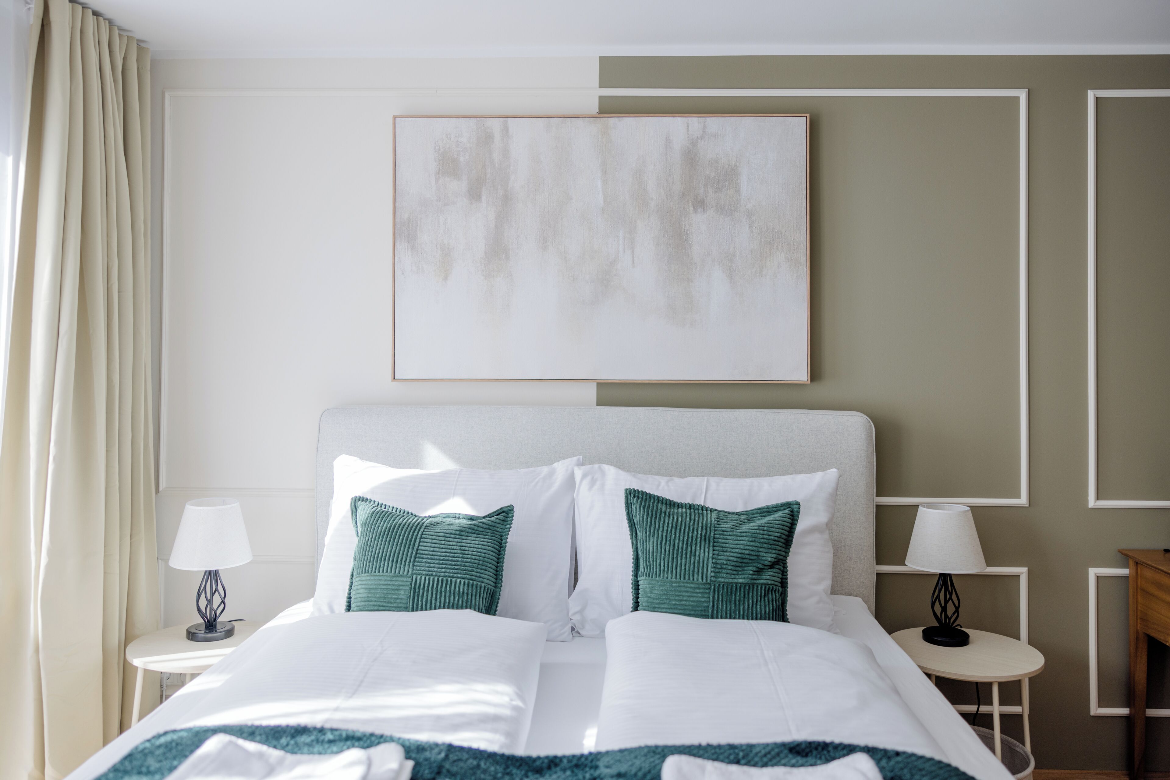 Habitación de hotel con una cama grande, dos mesitas de noche con lámparas, un cuadro en la pared y vistas al exterior.