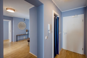 Un pasillo con piso de madera, un adorno circular en la pared, una mesita con un florero y una puerta con cortina.