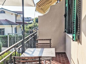 Ein Balkon mit Tisch und zwei Stühlen, einem Geländer und Blick auf benachbarte Gebäude.