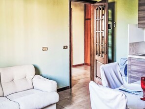 Ein Zimmer mit einem weißen Sofa, einem Esstisch mit einem Weinglas und einer Tür mit einem Metallgitter.