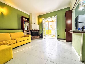 Ein Wohnzimmer mit einem gelben Sofa, einem Kamin und einer Glastür, die zu einem Außenbereich führt.