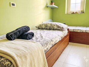 Ein ordentlich gemachtes Bett mit einer gemusterten Tagesdecke, zwei Kissen, einem aufgerollten Handtuch und einer beigen Zudecke.
